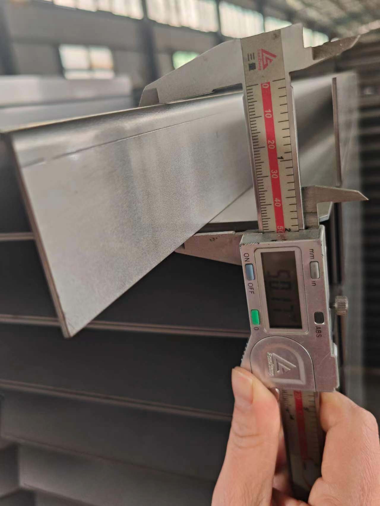 A worker is measuring the width of metal plate with calliper.